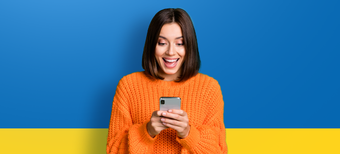 Imagem mostra uma mulher feliz ao olhar para o smartphone em suas mãos